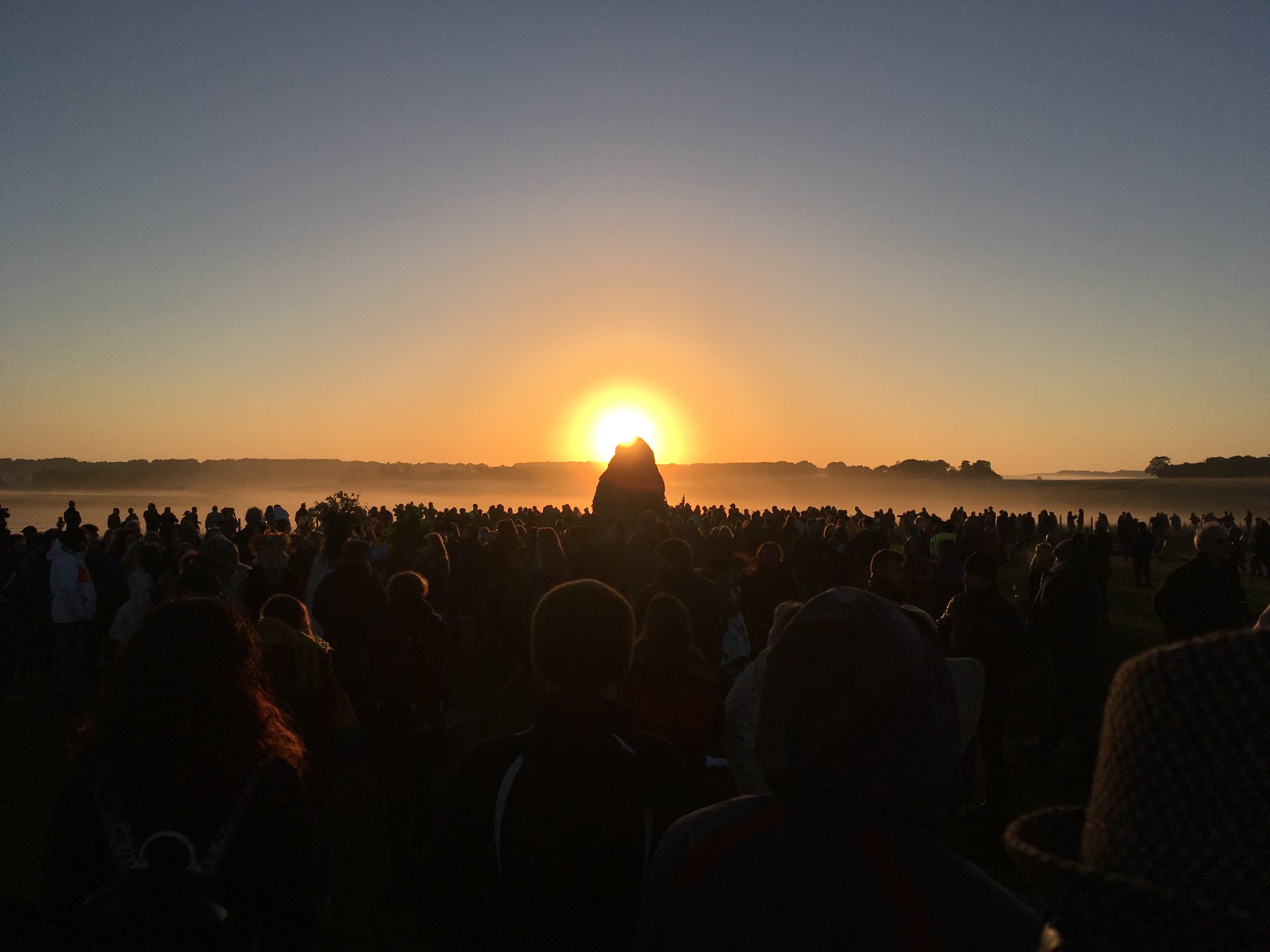 a crowd of people all standing close together, while the sun rises in the distance.