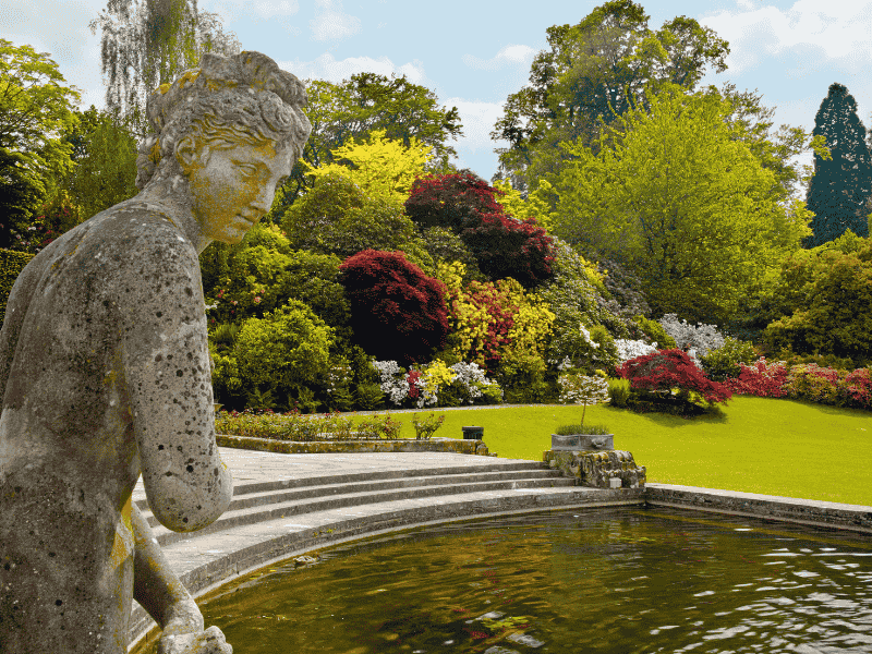 The Half Moon Pond at Hever Castle Gardens with a stone statue and colourful seasonal flowers — featured on the Anderson Tours Leeds and Hever Castle Day Tour from London.