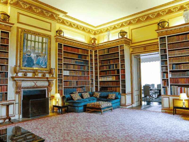 The Library at Leeds Castle with ornate bookcases, antique furnishings, and a grand portrait above the fireplace — featured on the Anderson Tours Leeds and Hever Castle Day Tour from London.
